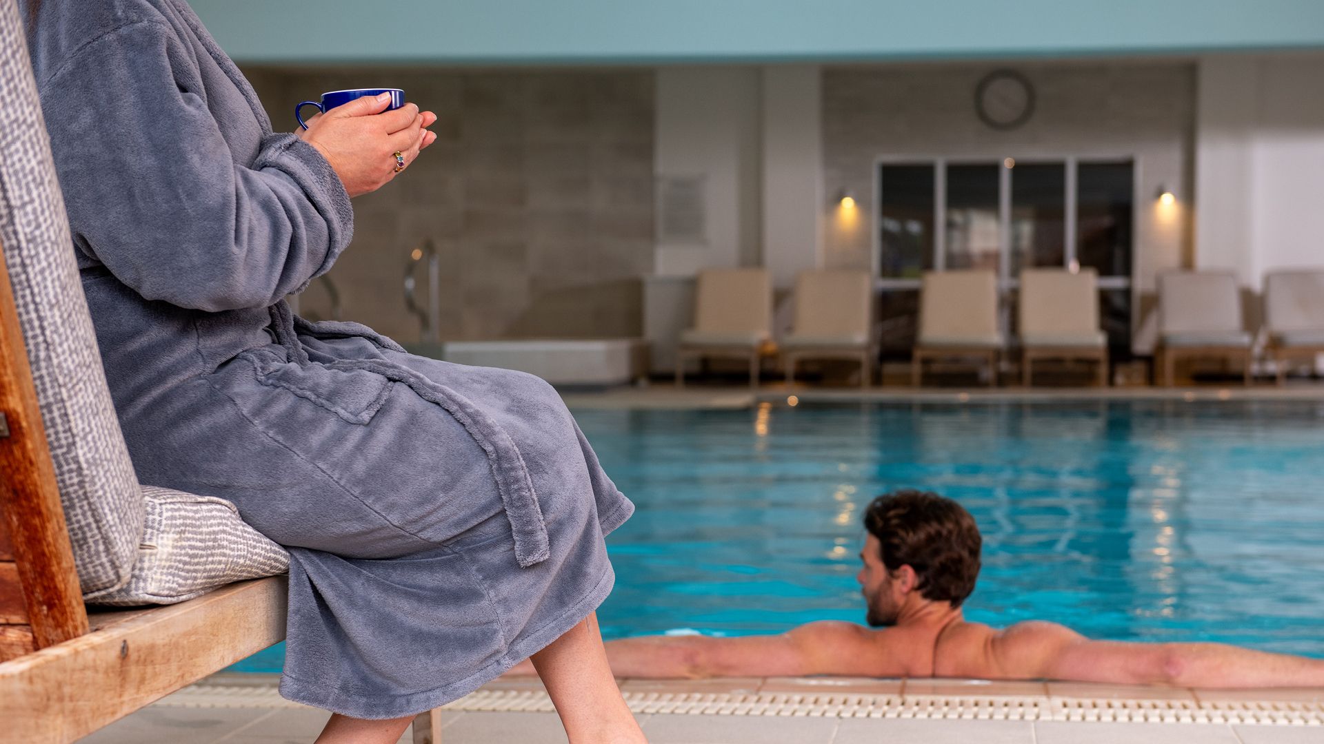 Man in pool, woman to the left enjoying a warm drink